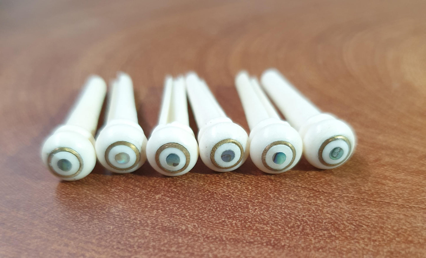 1 set (6pcs) Guitar bridge pins Bone with brass and Paua dot.Tapered shaft string slot running the full length of shaft. Diameter at top of shaft 5.35mm (0.21") length of shaft 25.4mm (1") . Will fit most guitar models.