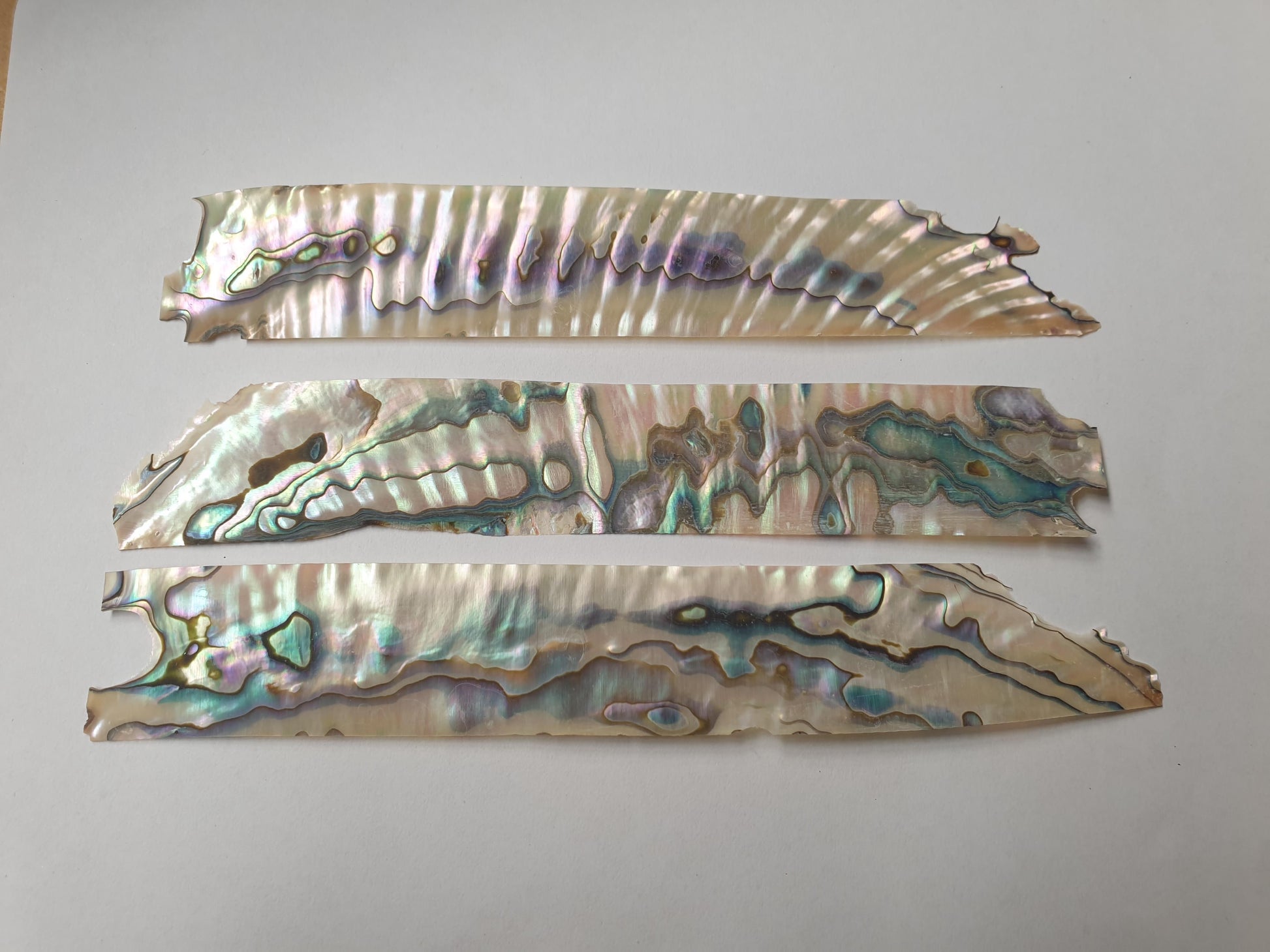 <p>Green abalone shell feathers 23mm (0.9") width x 120-150mm (4.72-5.9") length x 0.15mm (0.006") thickness - thinly sliced solid shell pcs. Cut along the curved part of shell then flattened, they can yield larger pcs then standard solid shell blanks. Ideal for shallow inlay, overlay, fishing lure manufacture and other decorative purposes. Select quality A grade.</p>