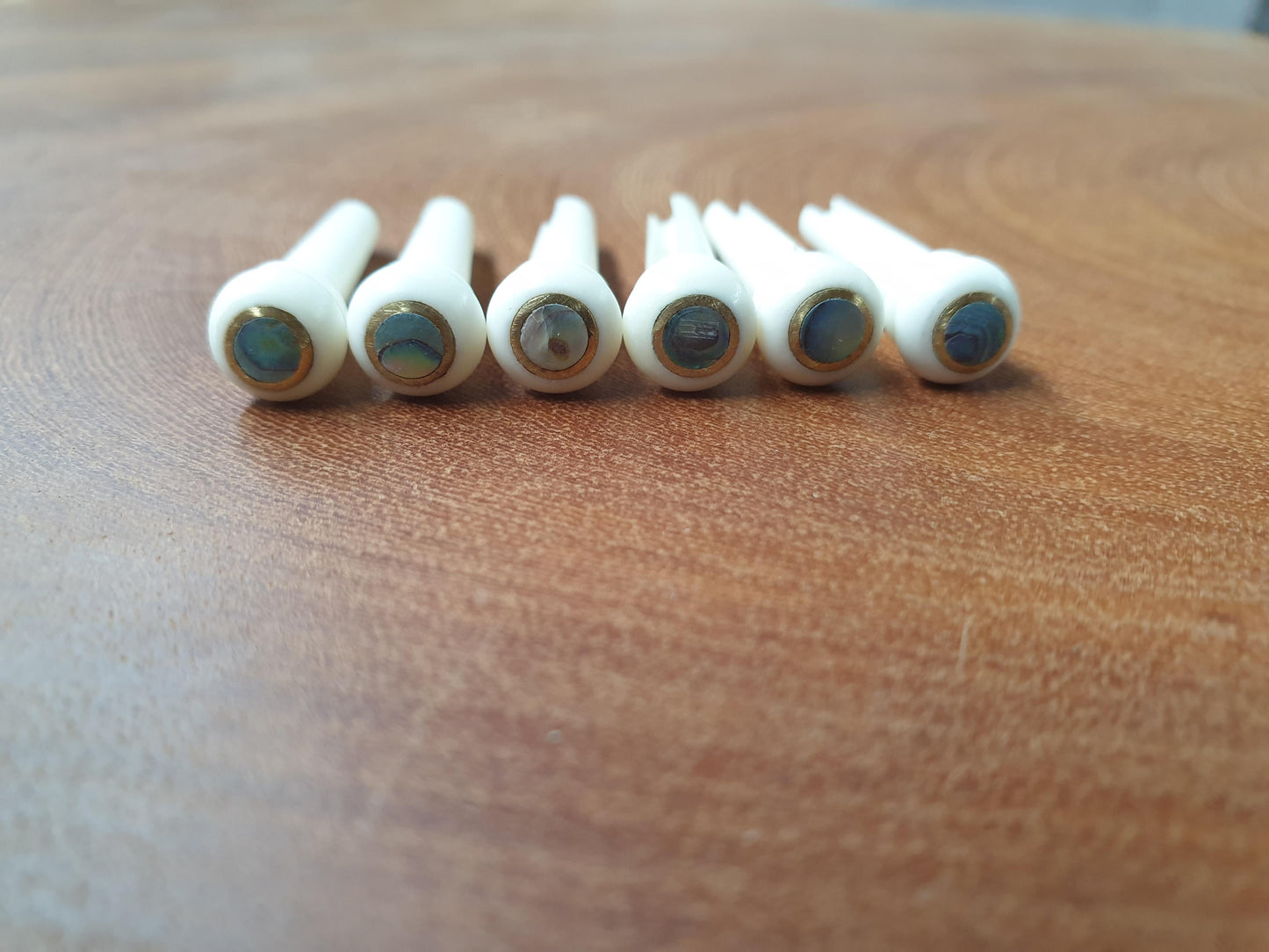 1 set (6pcs) Guitar bridge pins Bone with brass and Paua dot.Tapered shaft string slot running the full length of shaft. Diameter at top of shaft 5.35mm (0.21") length of shaft 22mm (0.866") . Will fit most guitar models.